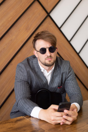 A young man in a suit and sunglasses is sitting in the office and looking at the phoneの写真素材