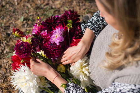 A cute girl is sitting on the street and holding an autumn bouquet of dahlias in her handsの写真素材