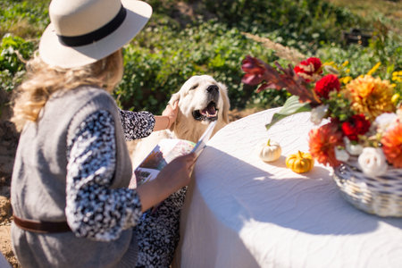 Cute girl in a hat reading a book and petting a labrador dogの写真素材