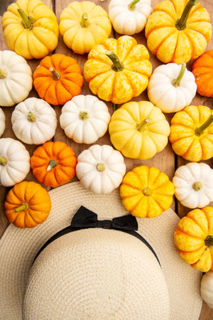 Yellow orange and white pumpkins are lying on a wooden table next to the hatの写真素材
