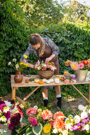 Cute florist girl collects a bouquet of autumn flowers in a basket on the tableの写真素材