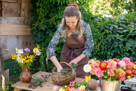 Cute florist girl collects a bouquet of autumn flowers in a basket on the tableの写真素材