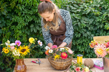 A florist girl collects a bouquet of autumn flowers in a basket on the streetの写真素材