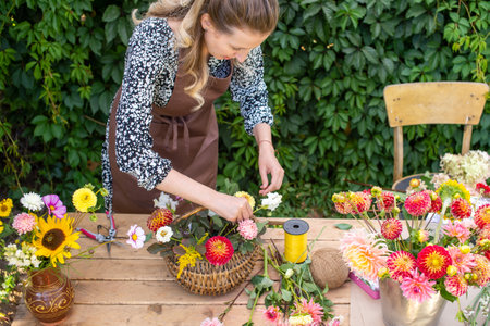 A cute florist girl collects a bouquet in a basket of autumn flowers on her desktopの写真素材