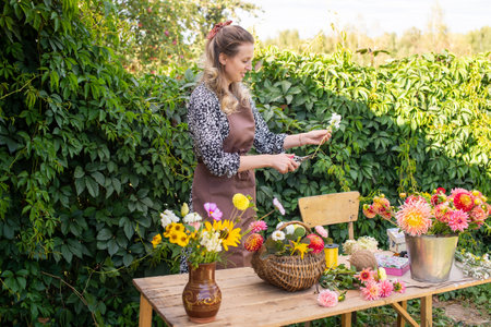A cute florist girl collects a bouquet in a basket of autumn flowers on her desktopの写真素材