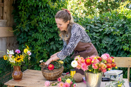 Cute florist girl collects a bouquet of autumn flowers in a basket on the tableの写真素材