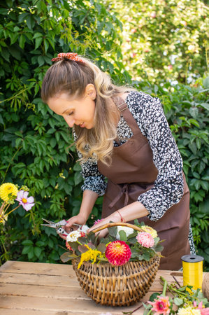 Cute florist girl collects a bouquet of autumn flowers in a basket on the tableの写真素材