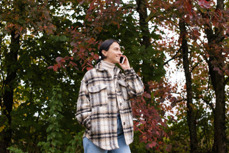 A girl in warm clothes is talking on the phone against the background of the forest and laughingの写真素材