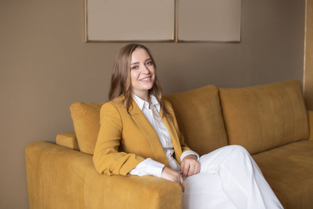 A cute girl in the office is sitting on the couch in a jacketの写真素材