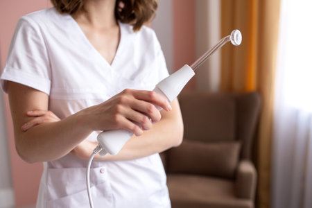 A female doctor holds a cosmetology electrical apparatus for cleaning the skin of the face
