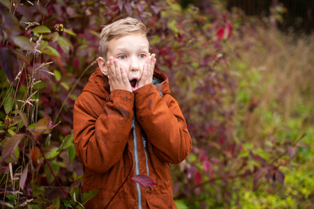 A cute boy in a red jacket looks away in surprise on the streetの写真素材
