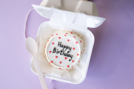 An open box with a bento cake and a wooden spoon for a birthday on a purple backgroundの写真素材