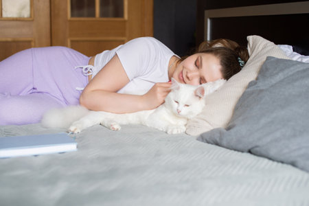 A cute girl is lying on the bed with her eyes closed next to a white catの写真素材