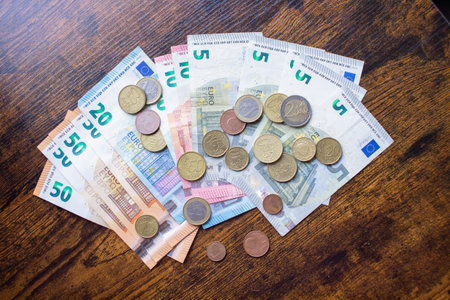 Euro banknotes of different denominations and coins lie on a wooden tableの写真素材