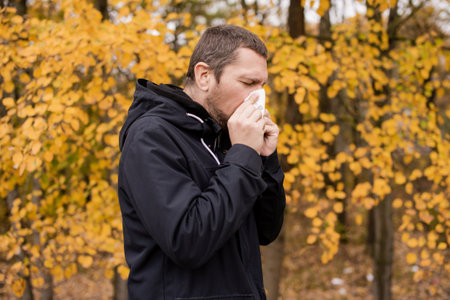 A man in a jacket is standing on the street and holding a napkin near his noseの写真素材