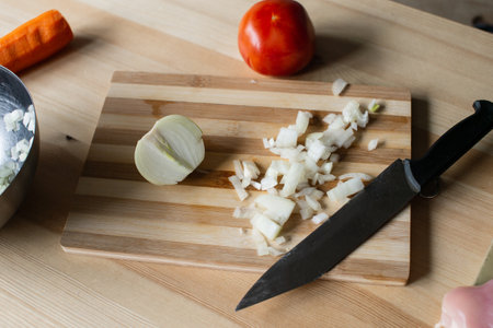 Diced onion lies on a cutting board with a knife and vegetablesの写真素材