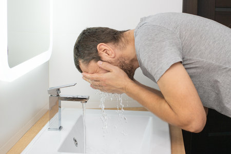 The man leaned over to the washbasin to wash his face with waterの写真素材