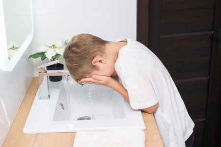 The boy bent down to the washbasin to wash himself with waterの写真素材