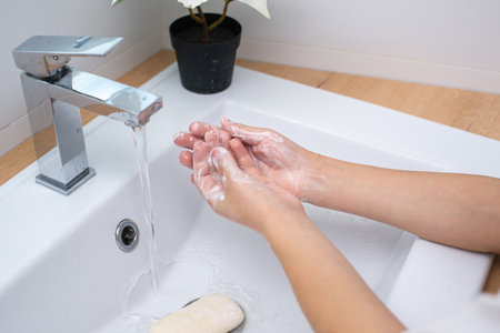 Soapy hands of a child in the washbasin under a stream of water in foamの写真素材