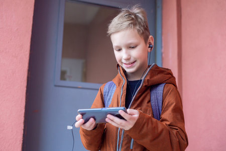 A cute boy is standing with a backpack and a phone with headphonesの写真素材