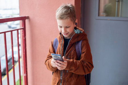 A cute boy is standing with a backpack and a phone , listening to musicの写真素材