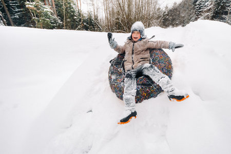 A happy boy is sitting in a tubing in the snow and riding down a slideの写真素材