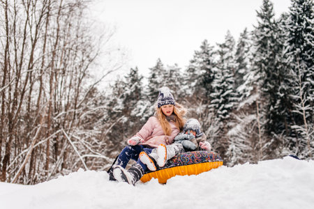 Brother and sister are sitting in a tubing in the snow and riding downhillの写真素材