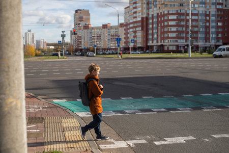 A boy with a backpack crosses the road at a pedestrian crossingの写真素材