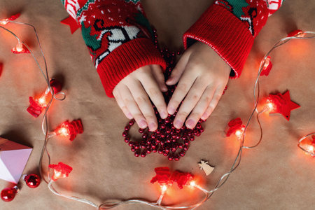 A red Christmas garland in children's hands lies on the tableの写真素材