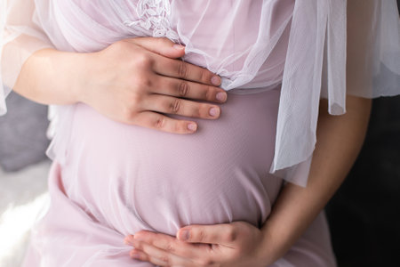 The belly of a pregnant woman in a pink dress holds her handsの写真素材