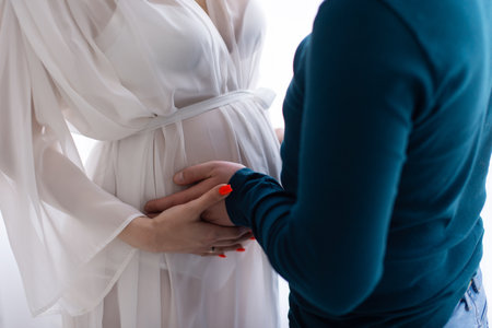 The belly of a pregnant woman in a bathrobe is held by male handsの写真素材