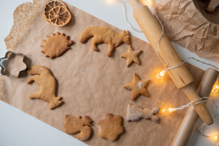 A frame of ginger cookies of different shapes on parchment, a rolling pin on the table and garlandsの写真素材