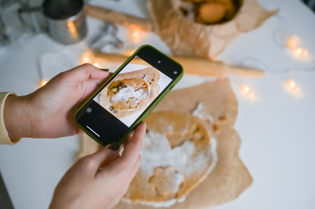 Hands with a phone take pictures of gingerbread dough with moldsの写真素材
