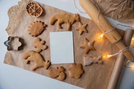 A frame with a white sheet of ginger cookies of different shapes on parchment, a rolling pin on the table and garlandsの写真素材