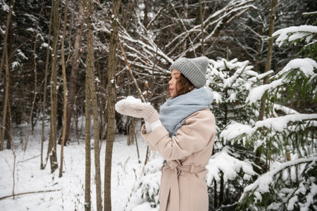 A cute girl in a hat and vazherzh holds snow in her hands and blows on itの写真素材