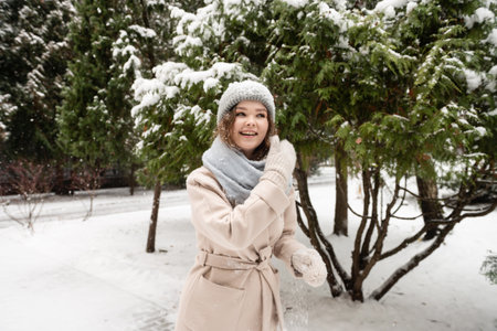 A cute girl laughs and removes snow from her hat with mittens in winterの写真素材
