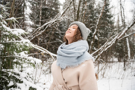 A cute girl stands under the snow with her eyes closed and smilesの写真素材