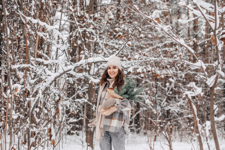 A cute girl in a hat walks in a snowy forest with branches of fir Nordic Trees Nobilis and smilesの写真素材