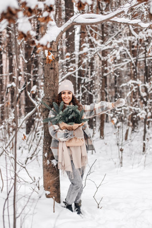 A cute girl in a hat walks in a snowy forest with branches of fir Nordic Trees Nobilis and smilesの写真素材