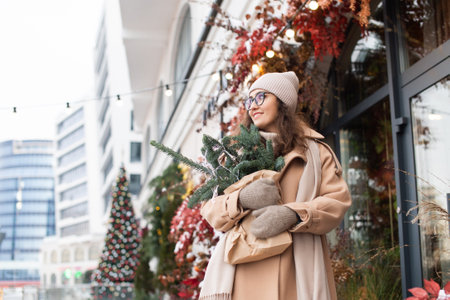 A stylish young woman wearing a hat with branches of nobilis in a craft bag walks around the Christmas cityの写真素材