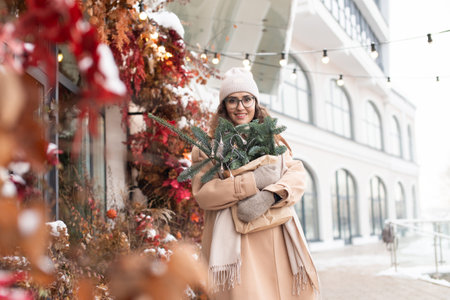 A stylish young woman wearing a hat with branches of nobilis in a craft bag walks around the Christmas cityの写真素材
