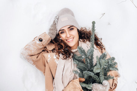 A cute girl with mittens and a hat lies in the snow with a package of fir nobilis and laughsの写真素材