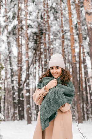 A cute girl has covered herself with a green scarf and is standing in the snow outside in winterの写真素材