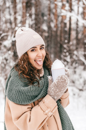 A smiling girl with a green scarf in winter in the forest holds a mug with snowの写真素材