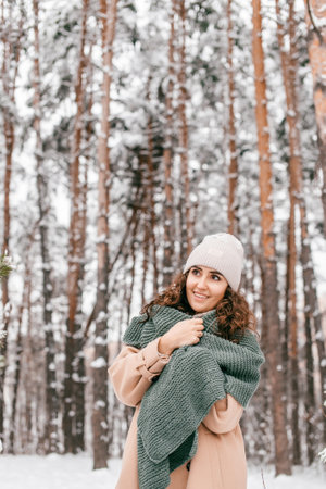 A smiling girl with a green scarf stands in a snowy forest in winter and looks awayの写真素材