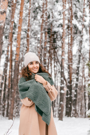A smiling girl with a green scarf in a coat stands in the snow in winter and looks awayの写真素材