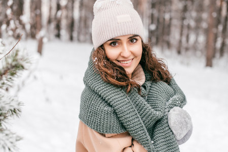 A cute girl has covered herself with a green scarf and is standing in the snow outside in winterの写真素材