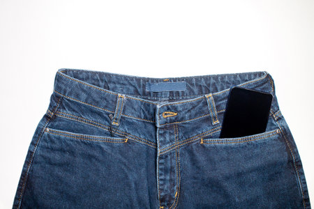 Denim trousers with an empty fabric label on a blue background. Classic front view of jeans on top with a phone in the pocket. Casual stylish clothes design of clothes and an empty background using copy spaceの写真素材