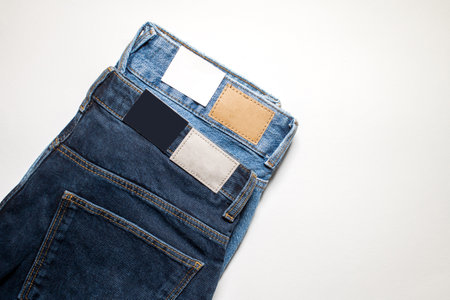 Two pairs of denim trousers with an empty leather label on a blue background.の写真素材