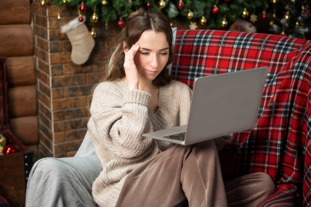 Cute girl experiences migraine and works on laptop at Christmasの写真素材